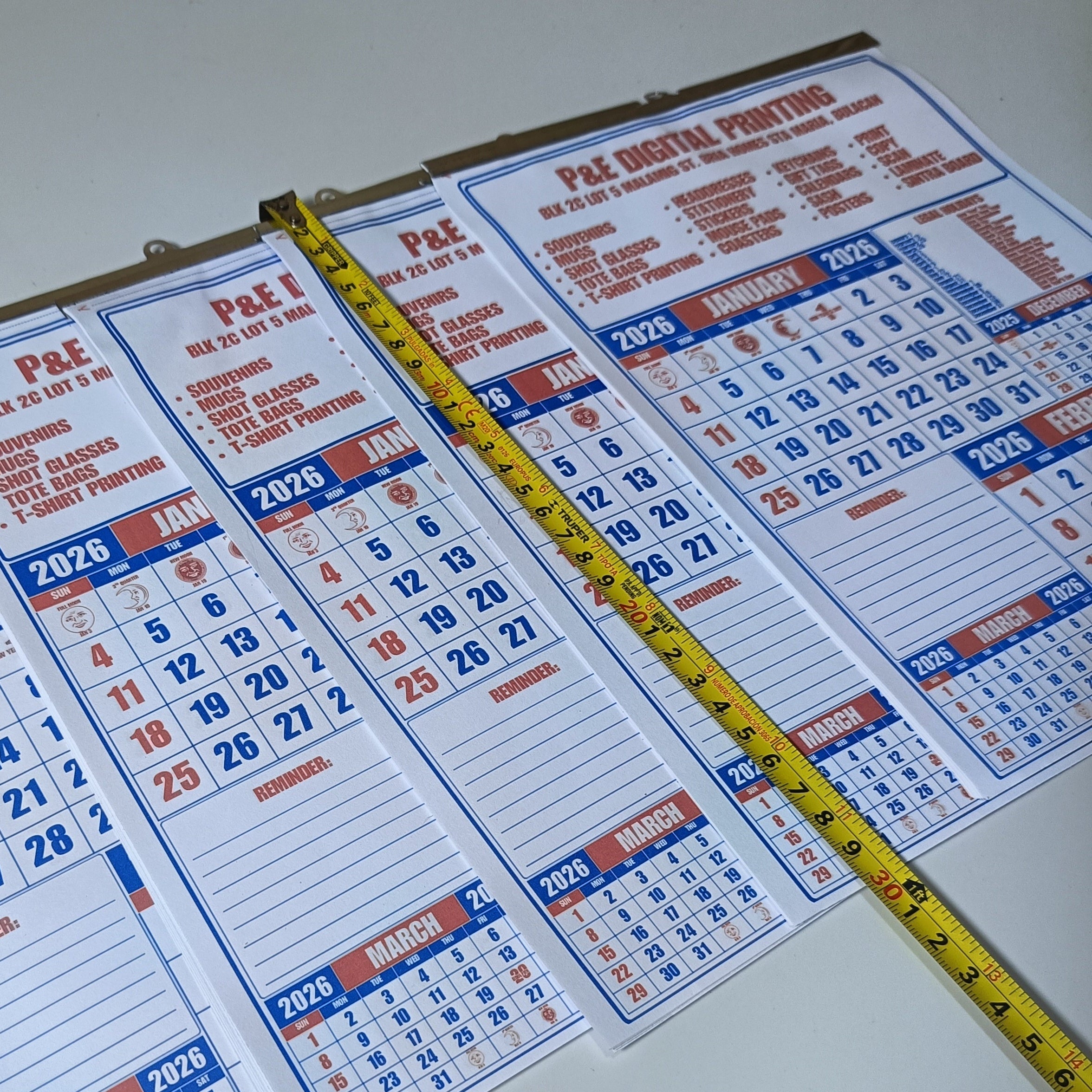 Calendar sheets with 2026 dates and a measuring tape for scale on a white background